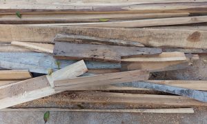 Stacked wood pieces lie scattered on dusty ground