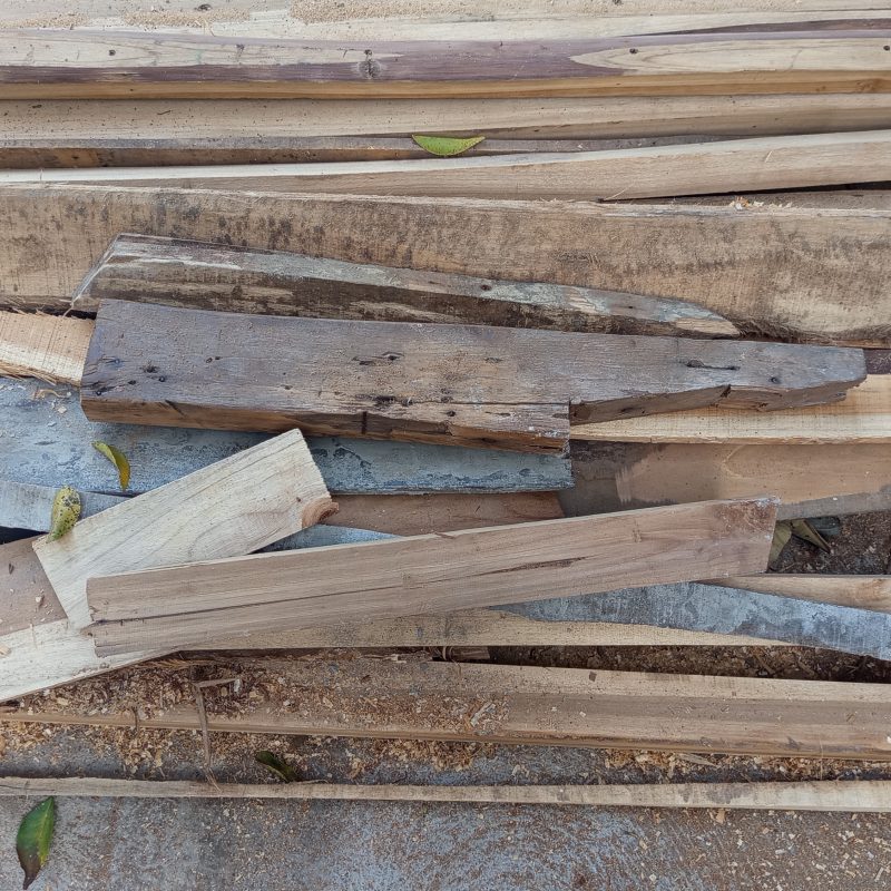 Stacked wood pieces lie scattered on dusty ground