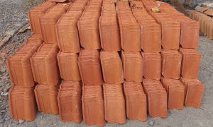 Stacked terracotta roof tiles lie on rough ground