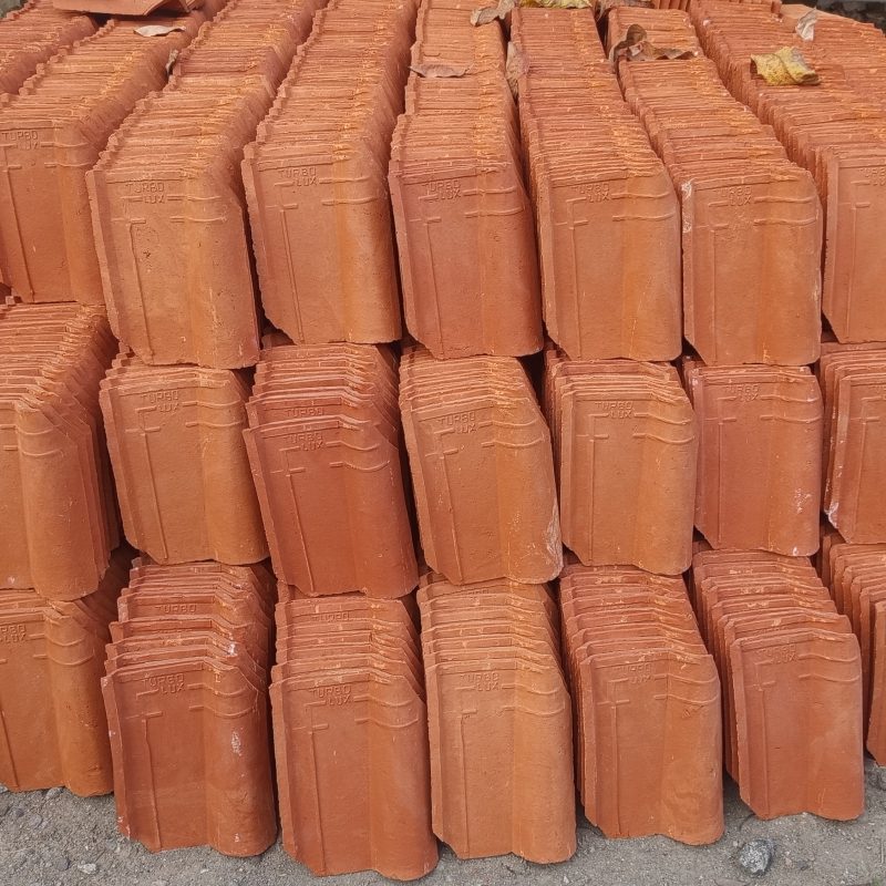 Stacked terracotta roof tiles lie on rough ground